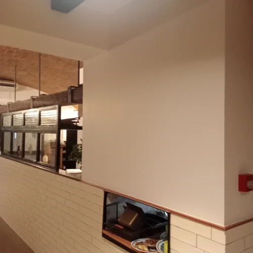 Imagen de un restaurante recién pintado con paredes blancas y detalles de ladrillo, iluminado por luces modernas.